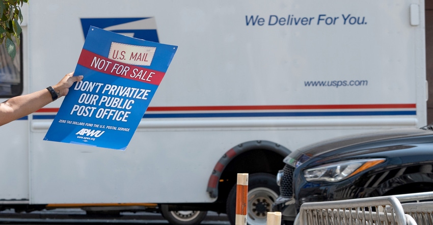 A woman holds a "U.S. mail not for sale" sign as a USPS mail truck drives past near at the "Save The Post Office" rally 