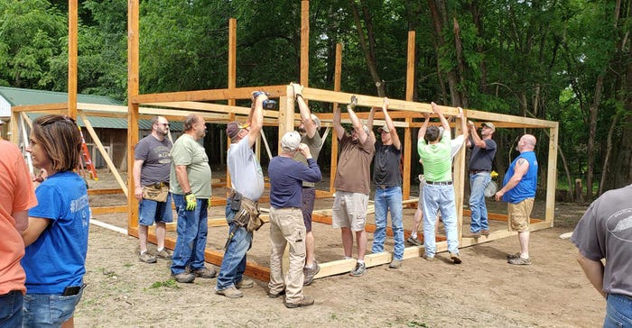 volunteers work to lift and secure the large beams for the barn 