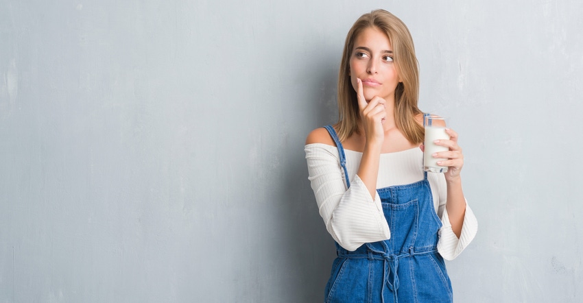 woman in overalls standing against gray wall holding a glass of milk