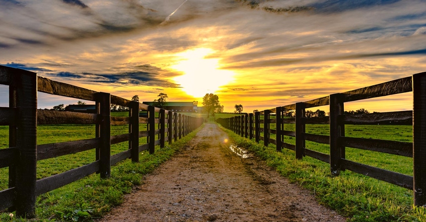 Dirt road leading to a barn with sunset