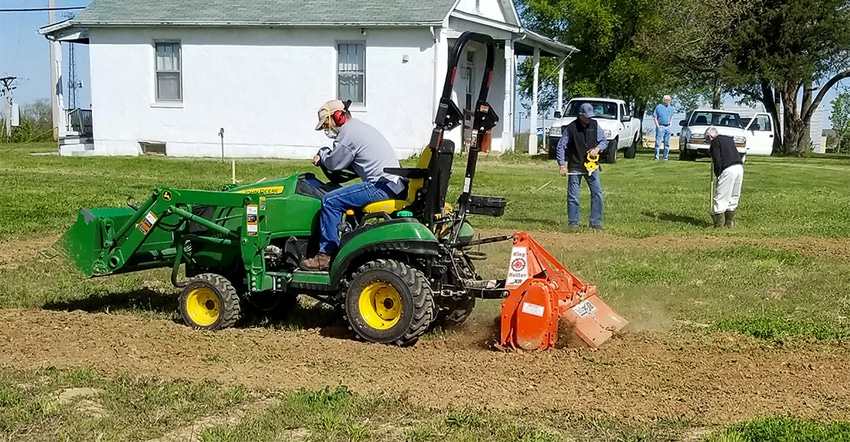 Man on tractor tilling soil near a church