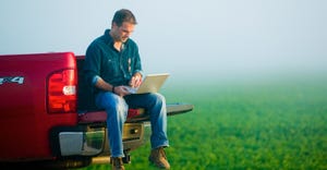 Farmer looking at laptop sitting on the tailgate of the truck