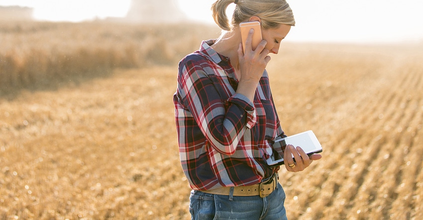 woman standing in harvested field with phone and tablet