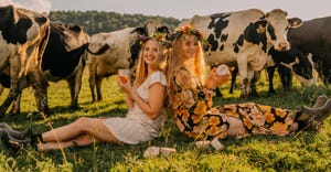 Stephanie and Hayley Painter holding containers of yogurt in field with dairy cows behind them