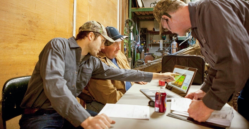 Three farmers looking over a computer while one of them points to the screen