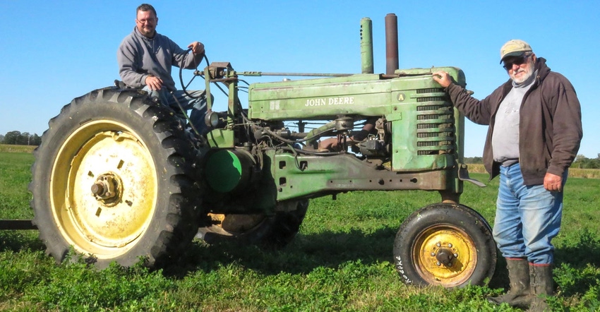 John Koepke sitting on a 1950 John Deere A tractor while Jim Koepke leans on the tractor posing for a photo