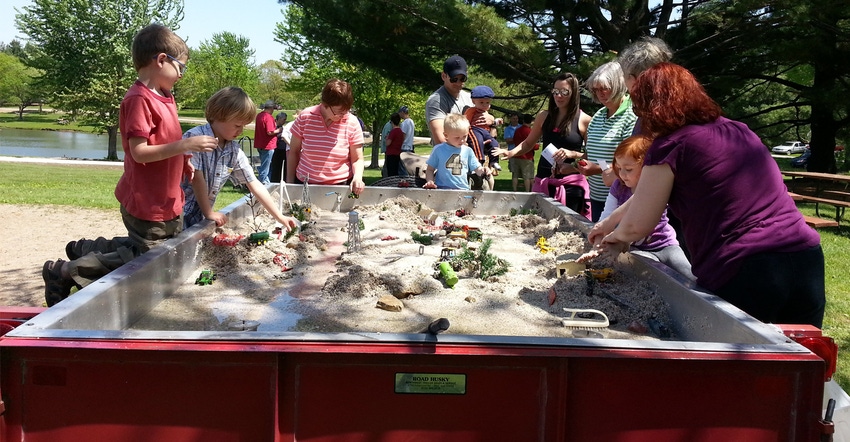 kids and parents playing in sandbox with tractors and farm equipment