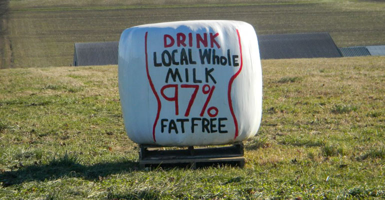 Plastic wrap on bale of hay in field reads 'Drink local whole milk 97% fat free'