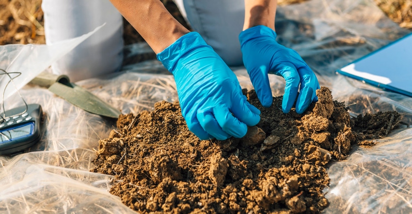Close up of gloved hands collecting soil samples from a field