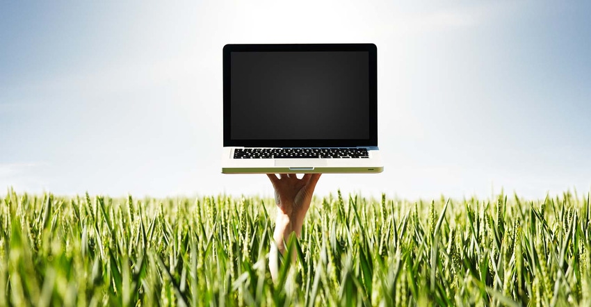 Hand holding up laptop through wheat field canopy