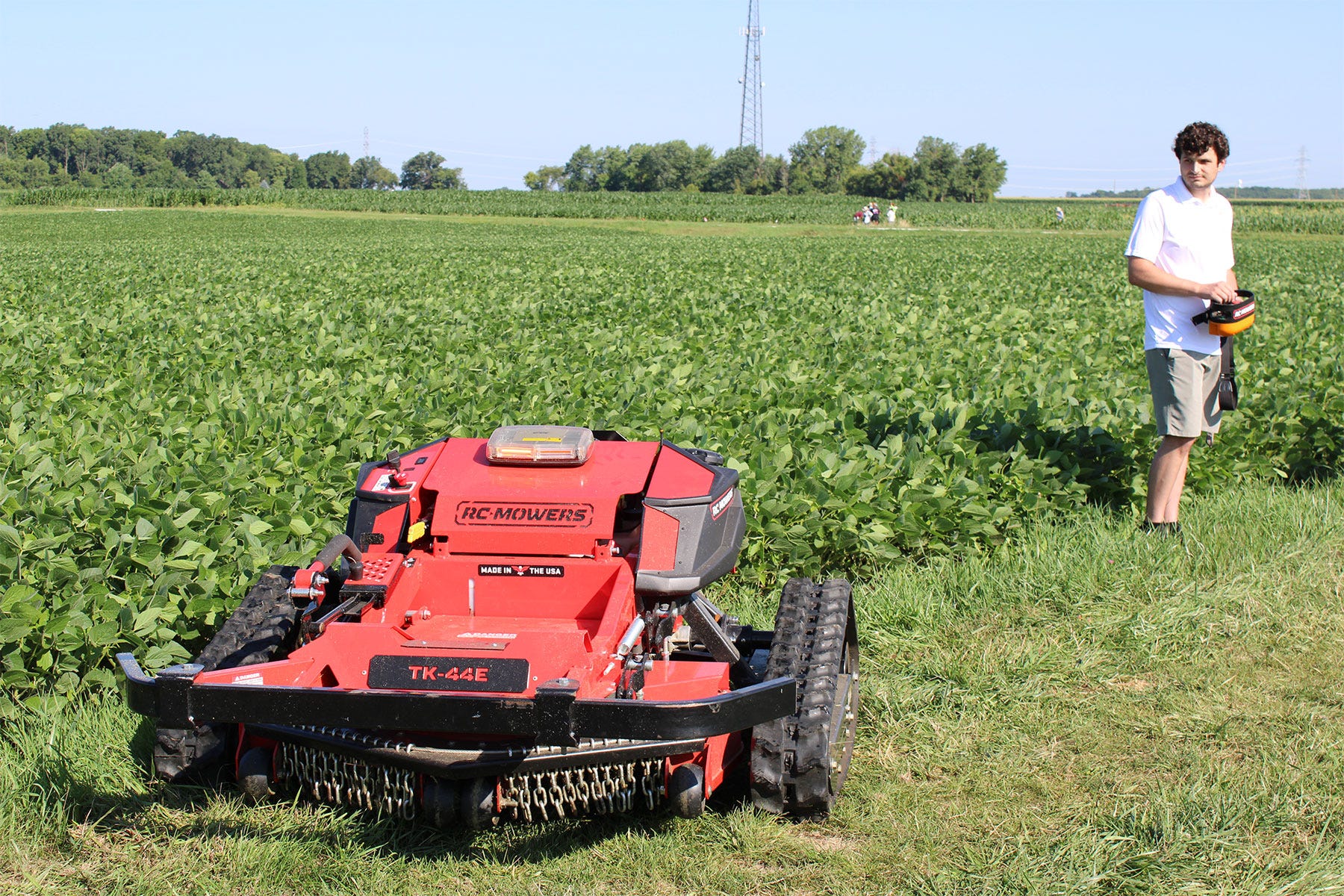 a college student demonstrates a red remote-controlled mower by a soybean field