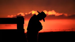 A silhouette of a cowboy with his head down with a sunset in the background