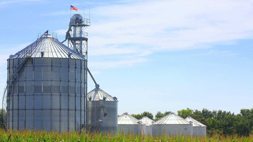 Grain bin setup with American flag next to corn field in late summer