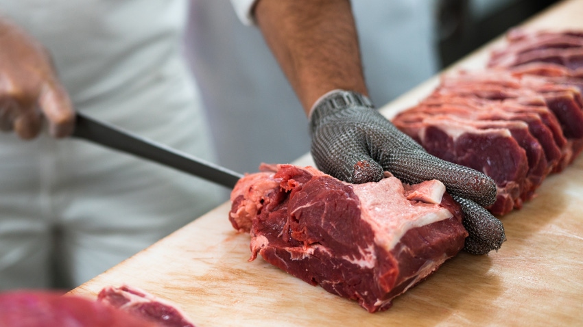 butcher wearing metal mesh glove slicing beef