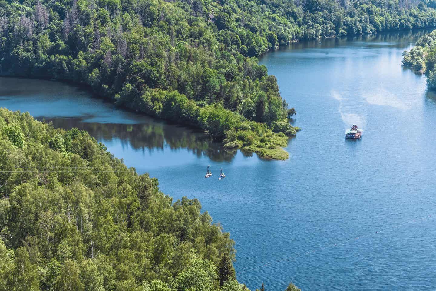 Blick auf den Stausee der Rappbodetalsperre, im Vordergrund zwei Menschen an einer Zipline 