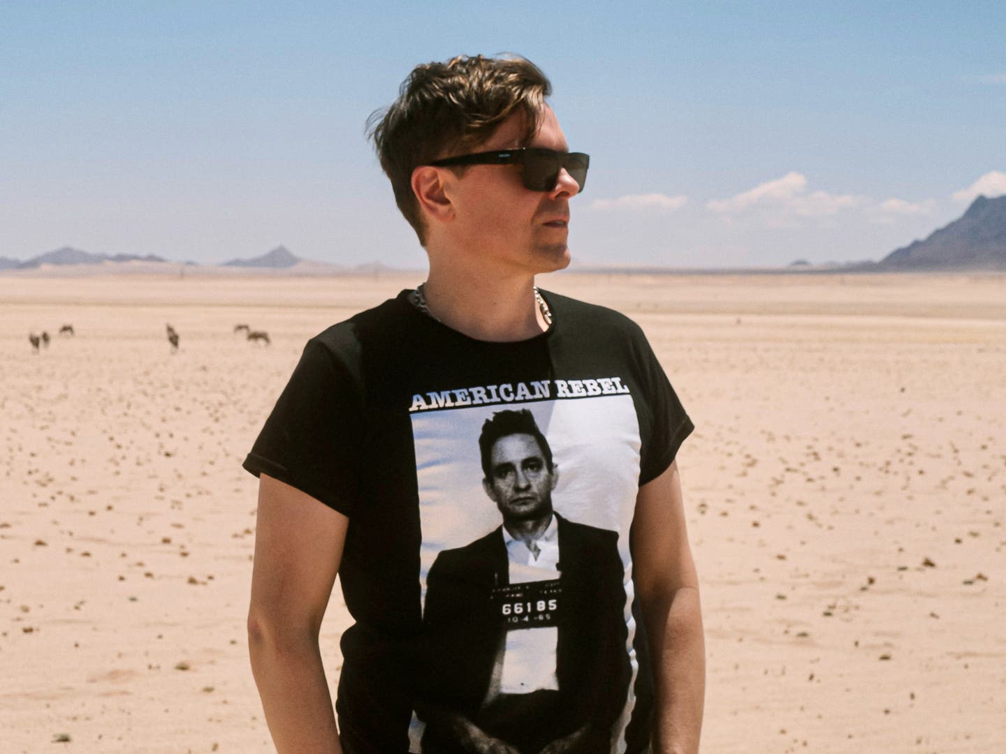 Foto von Michael Patrick Kelly, der mit einer schwarzen Sonnenbrille und T-Shirt in einer Wüste steht