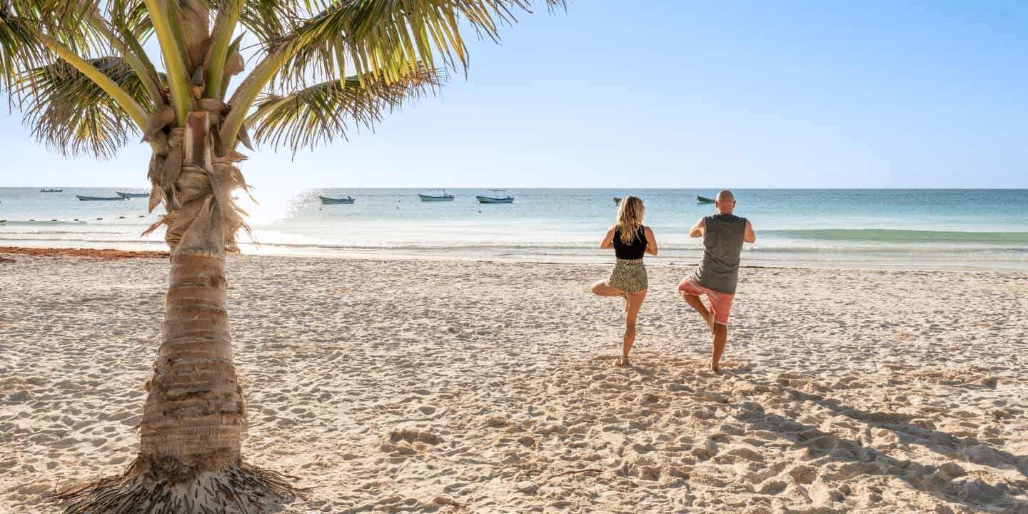 Strandurlaub in Mexiko: Ein Paar macht Yoga am Strand.