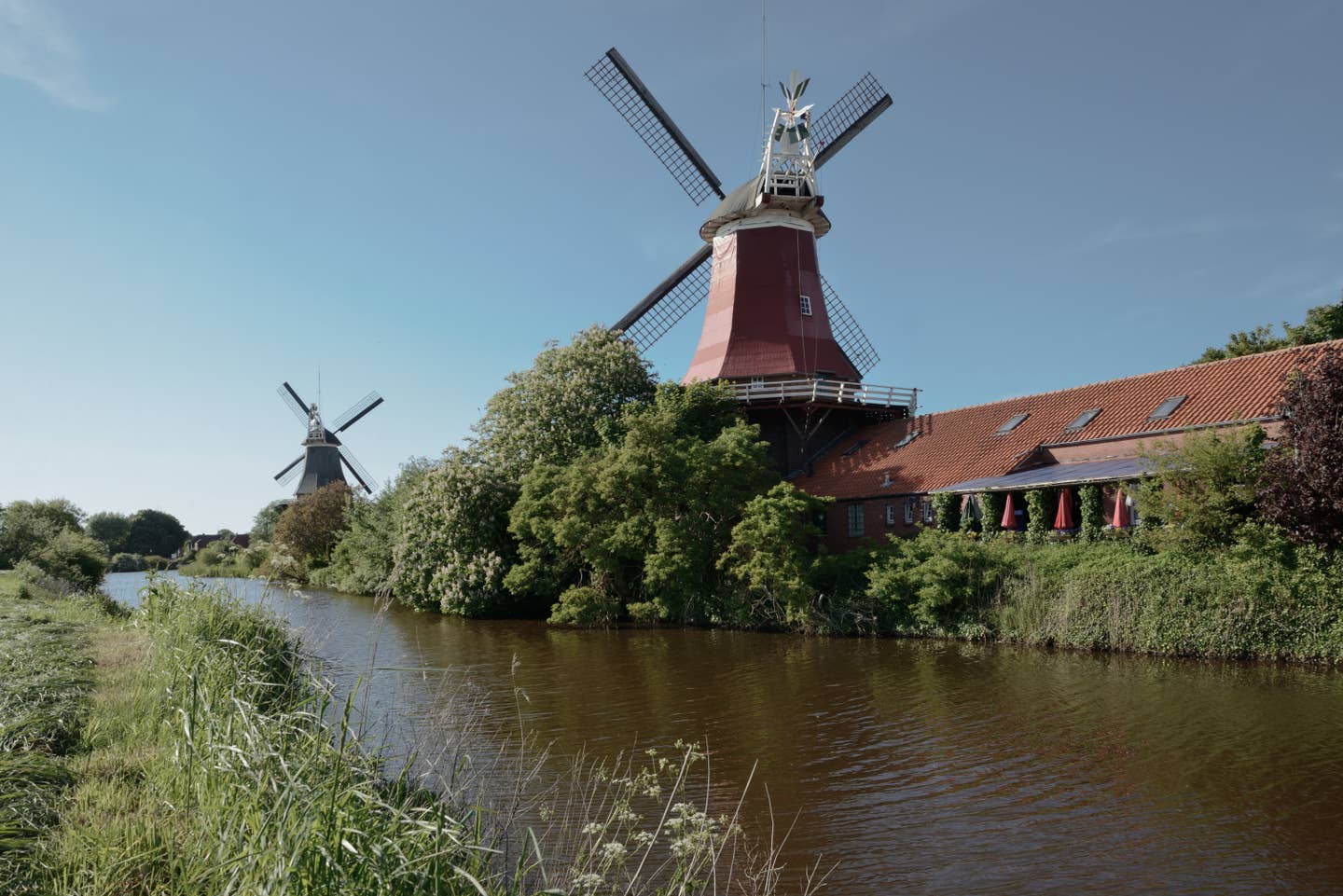 Niedersachsen Urlaub mit DERTOUR. Zwei Windmühlen an einem Fluss in Greetsiel, Ostriesland