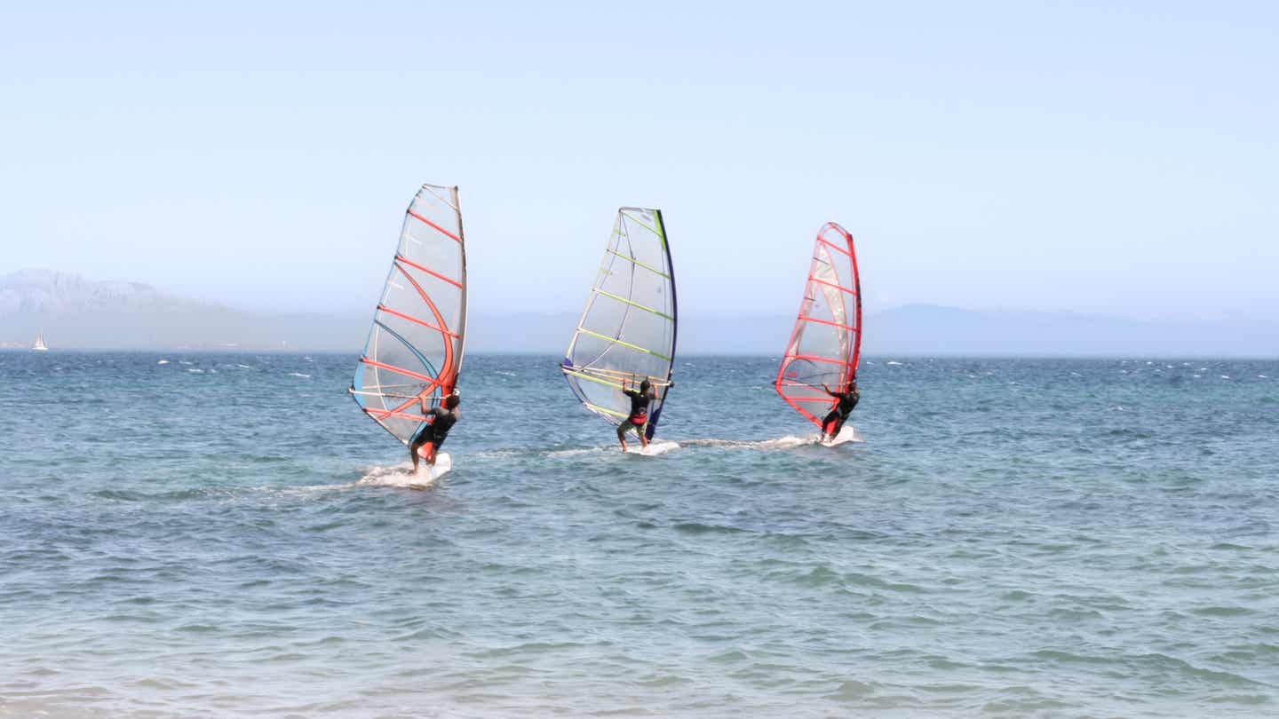 Tarifa surfen: Windsurfschüler mit bunten Segeln vor Punta Paloma bei ruhigen Bedingungen auf dem Wasser