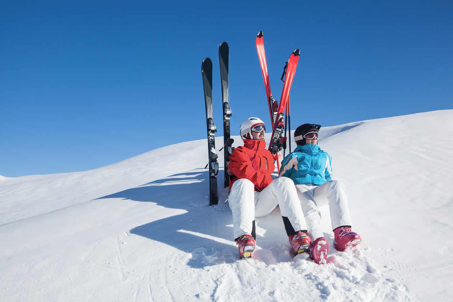 Paar sitzt mit Skiern im Schnee und macht eine Pause vom Skifahren im Schnee