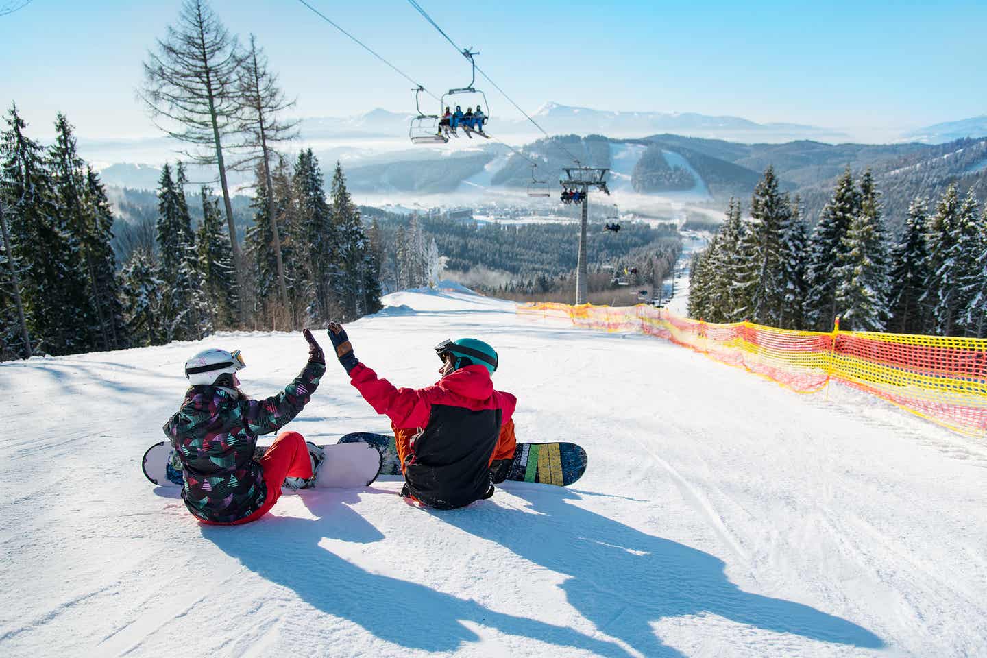 Snowboardersitzen mit dem Rücken zur Kamera auf einer Piste, die Sonne scheint