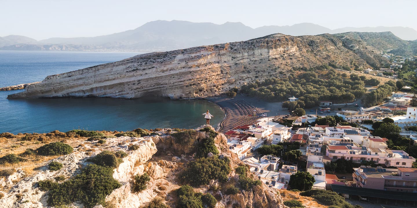 Instagram-Spots auf Santorini: Matala Beach auf Kreta mit Felsenküste, türkisblauem Wasser und Blick auf das Dorf im Abendlicht