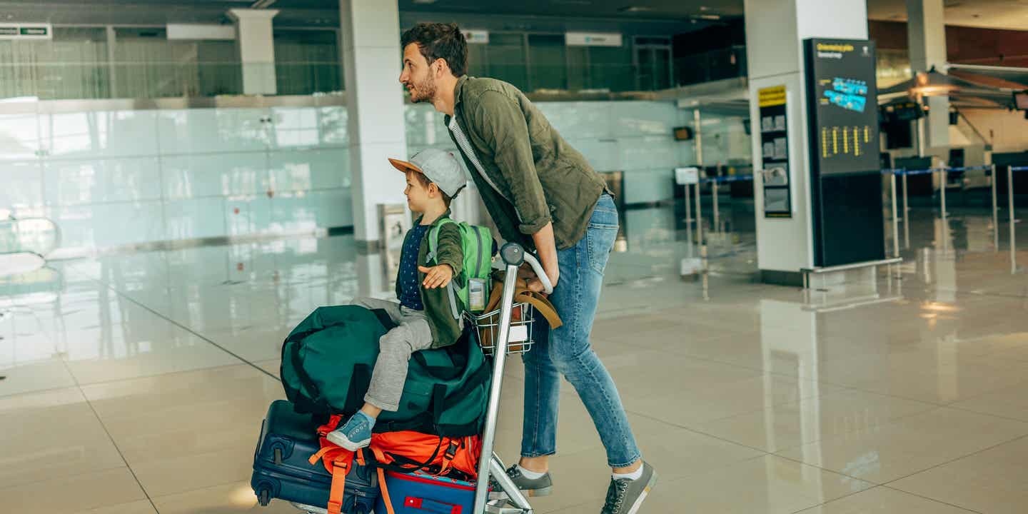 Packliste für Urlaub mit Kindern: Vater und Sohn mit einem Gepäckwagen auf dem Flughafen