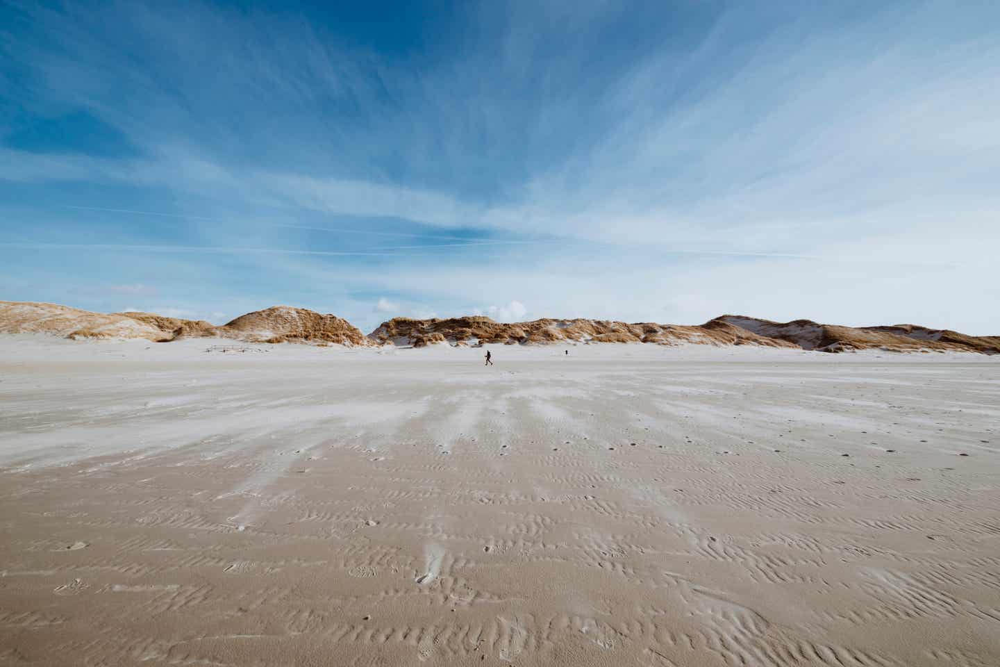 Breite Sandstrandlandschaft bei Ebbe mit Hügeln am Horizont bei mäßig bewölktem Himmel und Windspuren im Sand, Amrum, Deutschland - Please AL :)