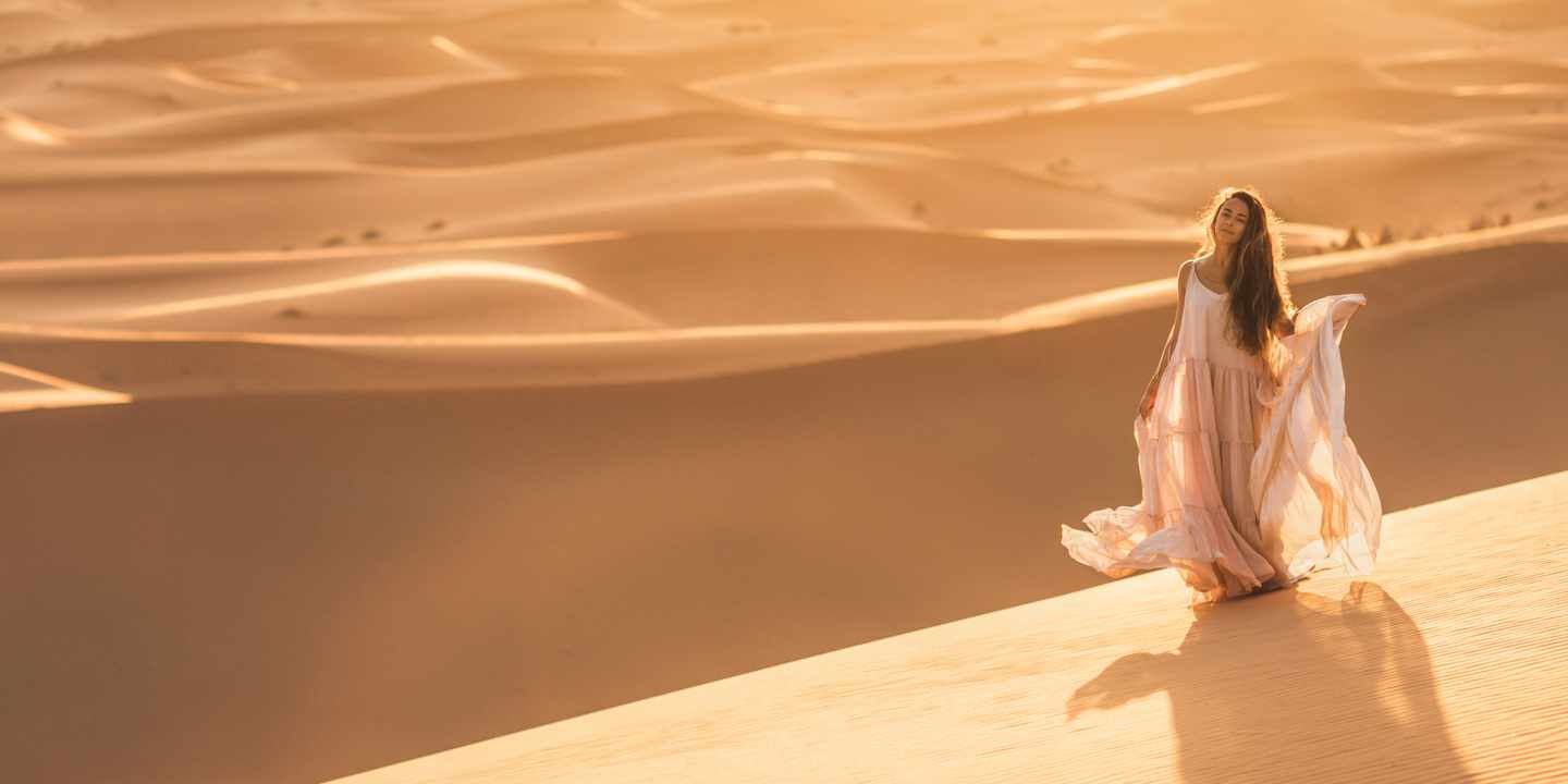 Frau im fließenden Kleid steht in der Sahara bei Sonnenuntergang – Main Character Energy Reise in Marokko