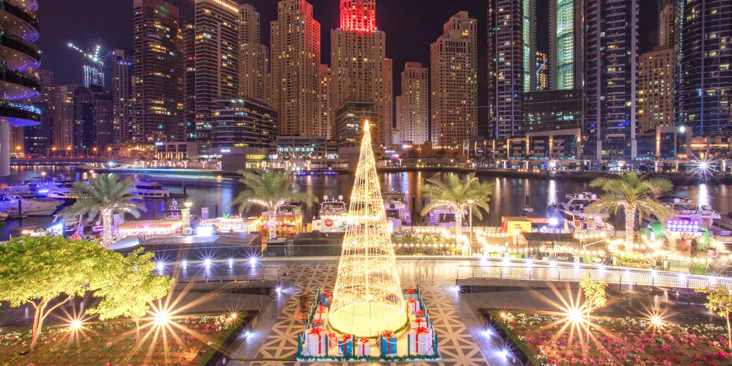 Blick auf einen aus goldenen Lichtern geformten Weihnachtsbaum vor Meer, Palmen und Skyscrapern