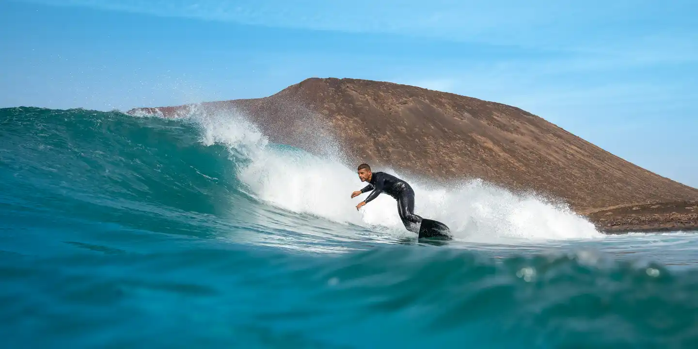 Surfer reitet eine Welle vor der Küste Fuerteventuras mit vulkanischer Inselkulisse im Atlantik