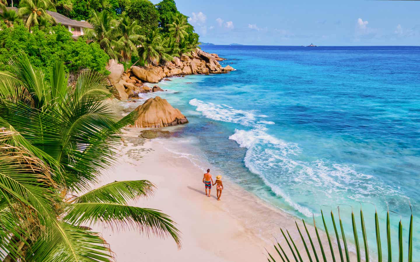 Paar spaziert am weißen Sandstrand von Anse Patates auf La Digue, Seychellen, mit Palmen und türkisblauem Ozean