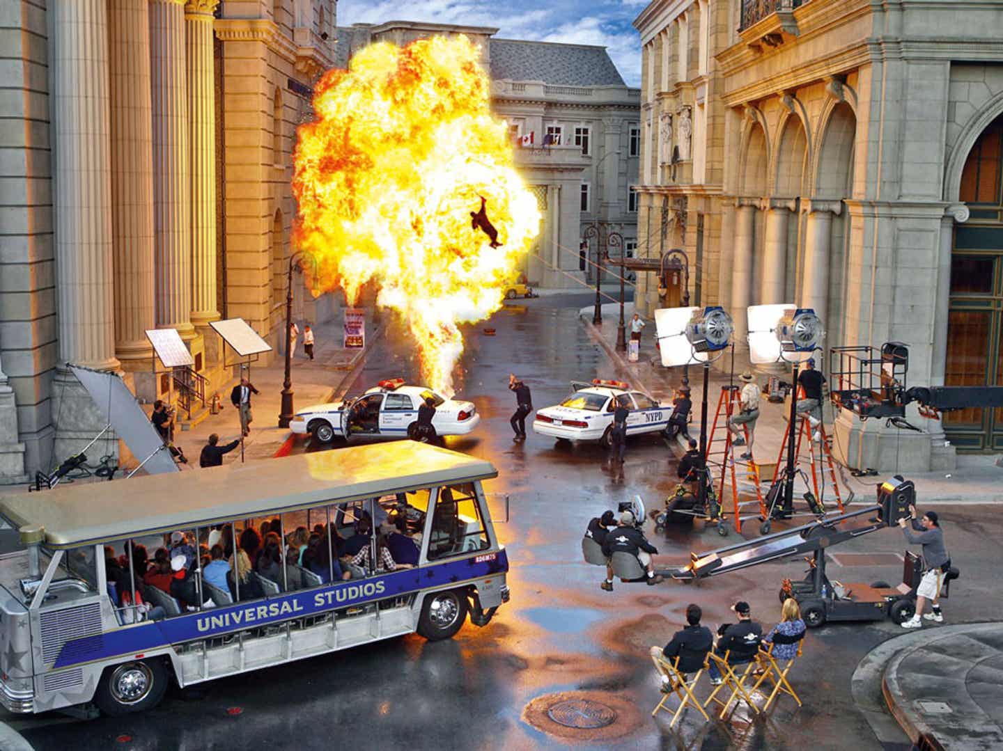 Blick auf die Los Angeles Sehenswürdigkeit Universal Studios mit Tourbus, Filmset und Actionszene an mit Explosion und Feuer an zwei Polizeiautos mit Cops.