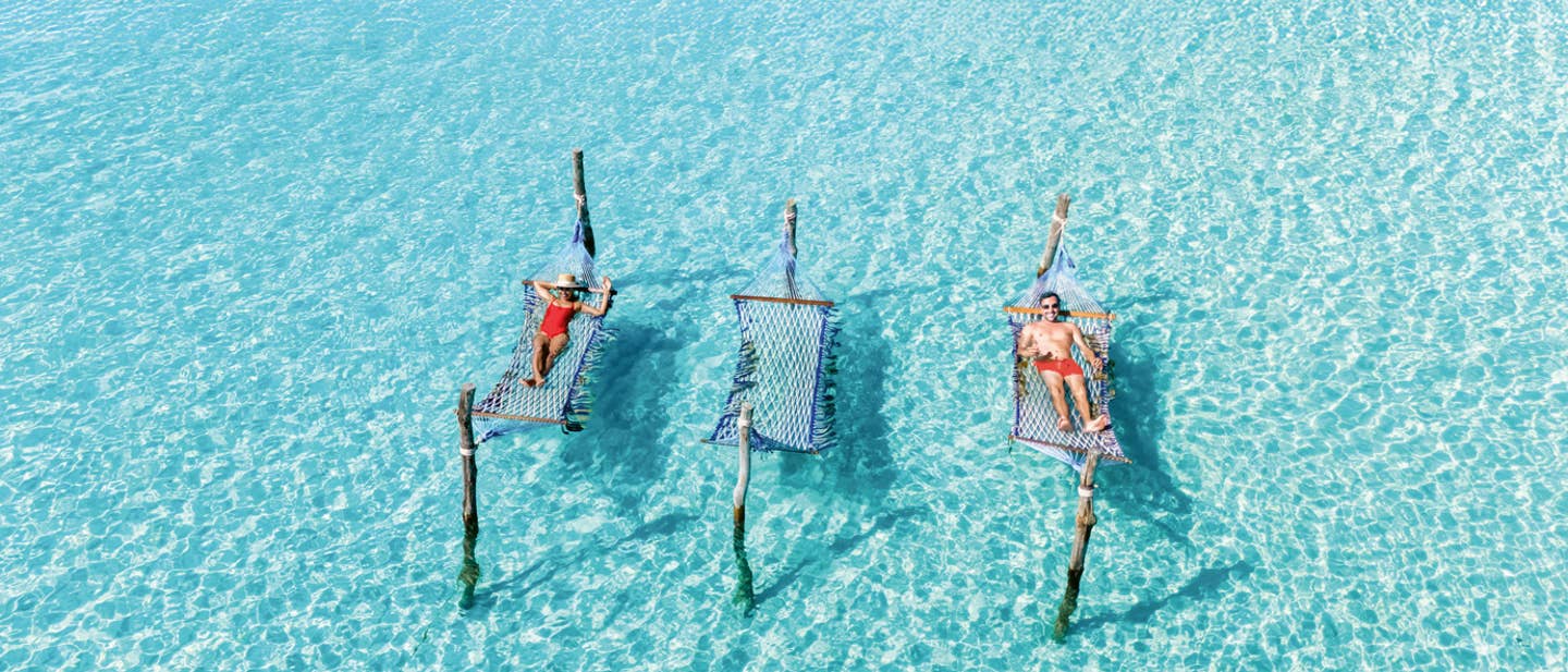 Frühbucherangebote 2026: Luftaufnahme von Personen in roter Badekleidung auf Hängematten im Wasser