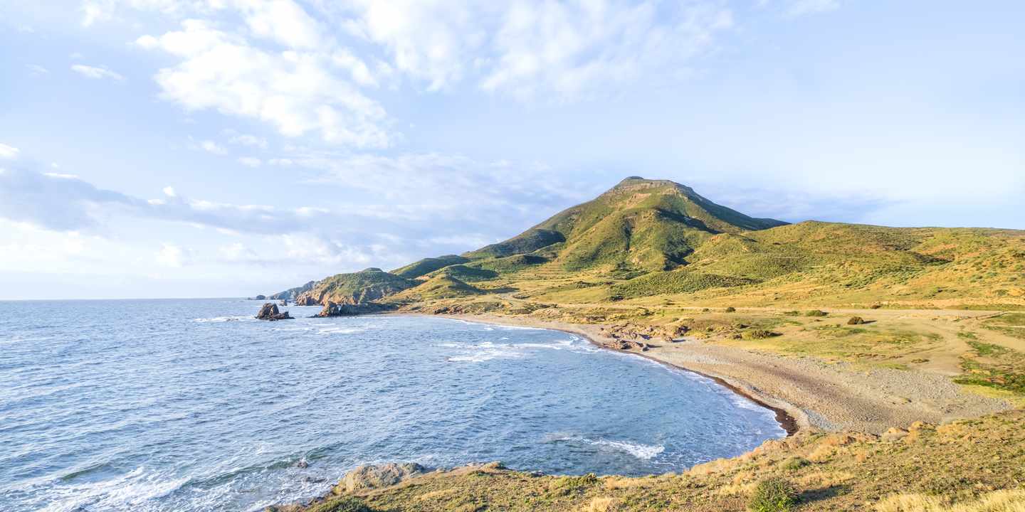 Küste im Cabo de Gata Naturpark mit Lavafelsen und heller Bucht unter blauem Himmel