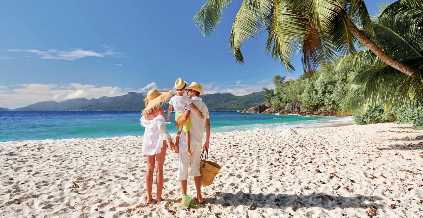 Familie im Seychellen-Urlaub an einem weißen Sandstrand mit grüner Palme