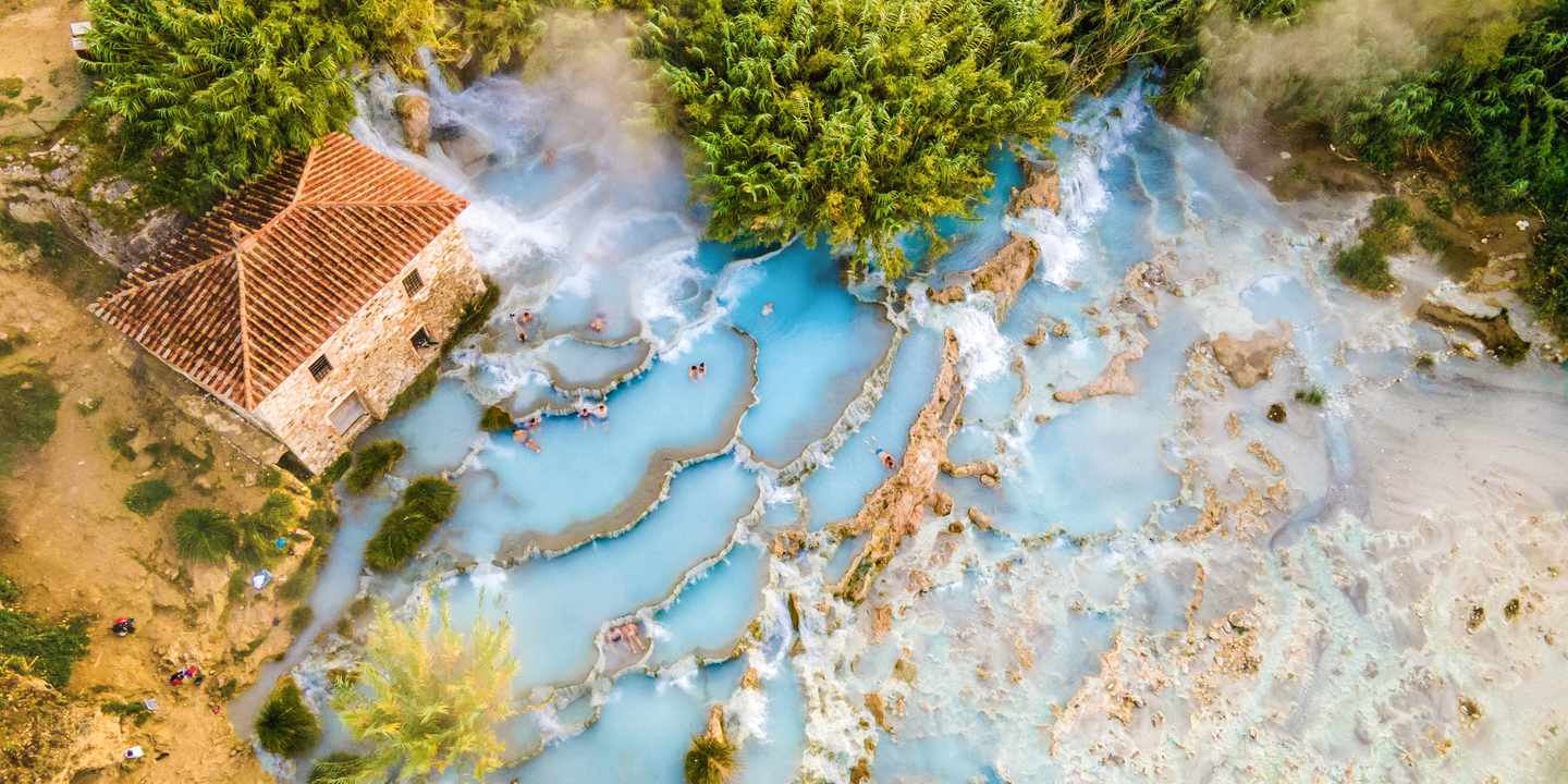 Vogelperspektive auf kleines Steinhaus mit rotem Dach neben Naturthermen in der Toskana