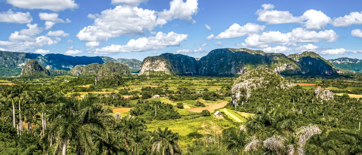 Kuba Reisetipps: Valle de Vinales Tal mit grüner Vegetation und markanten Kalksteinfelsen unter blauem Himmel mit Wolken