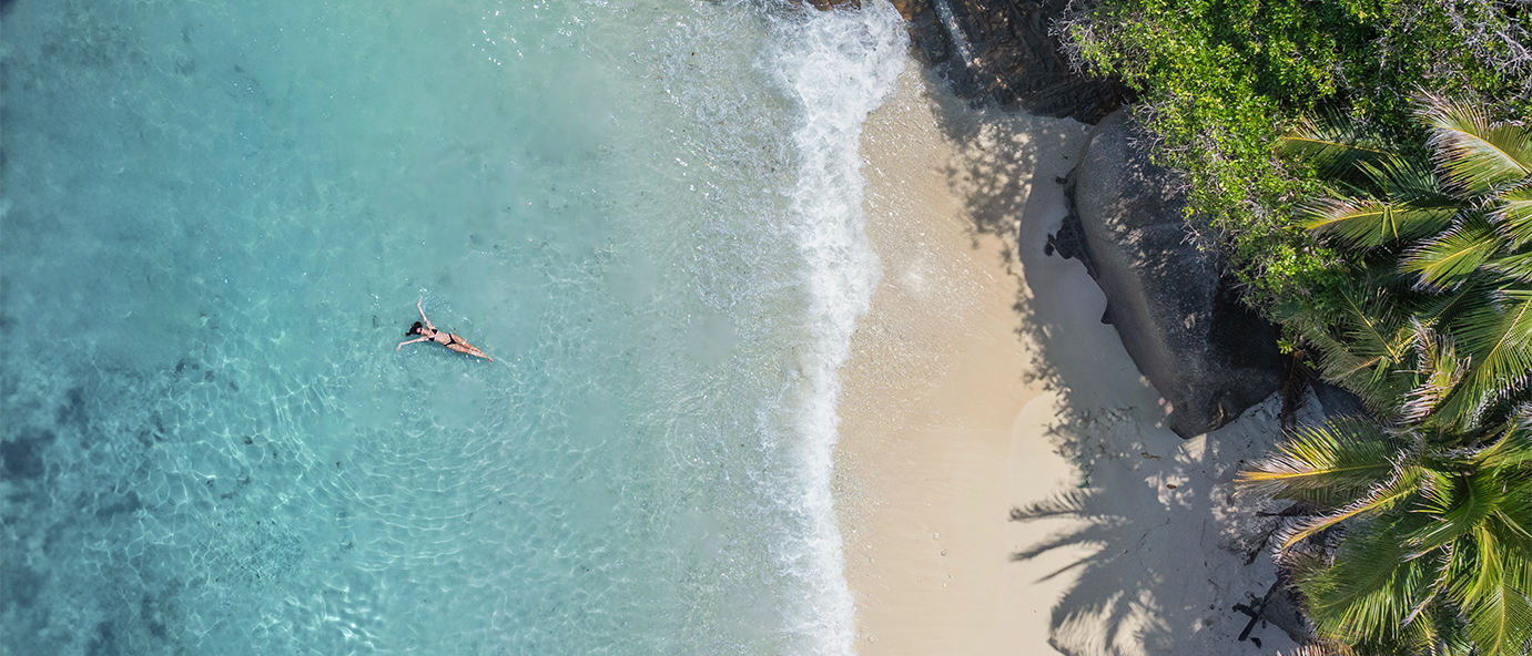 Sommerurlaub: Luftaufnahme einer Frau im türkisen Wasser auf den Seychellen