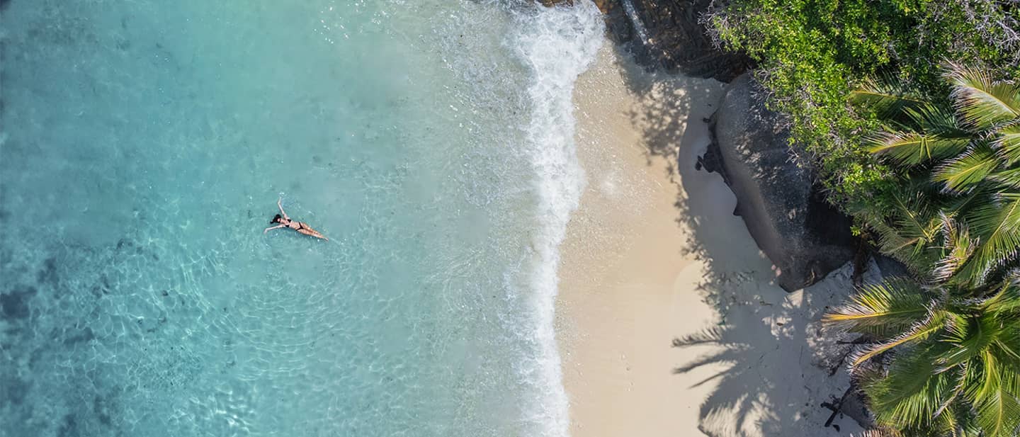 Sommerurlaub: Luftaufnahme einer Frau im türkisen Wasser auf den Seychellen Sommerurlaub: Luftaufnahme einer Frau im türkisen Wasser auf den Seychellen