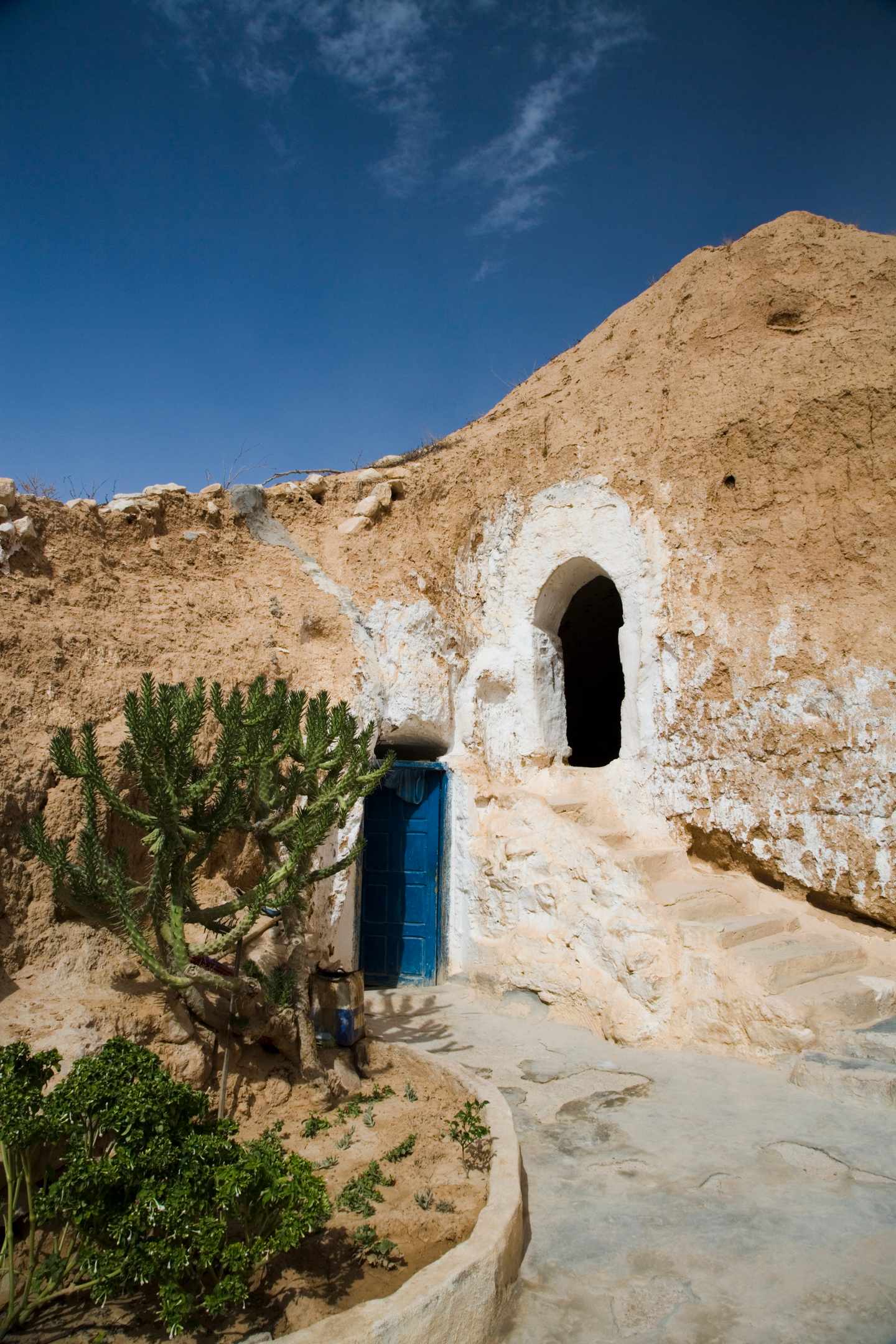 tunesien-matmata-troglodytenhaus-hoehlenhaus-eingang-g-174905628.jpg Eingang zu einem traditionellen Troglodytenhaus in Matmata, in den Fels gebaut, mit weiß verputzter Fassade und blauer Tür