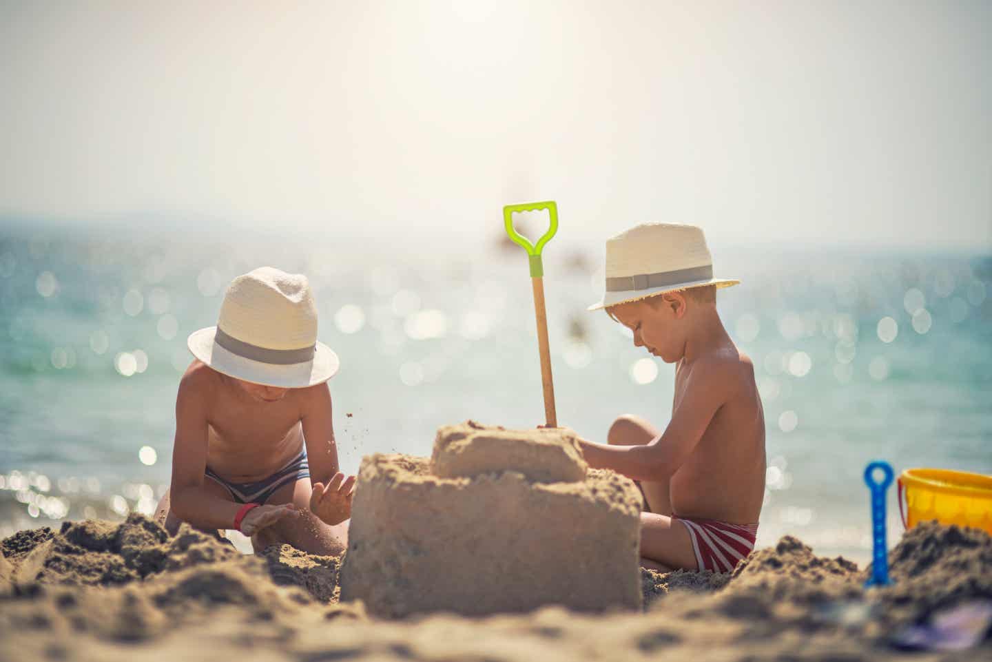 Zwei Kinder bauen im Familienurlaub auf Mallorca eine Sandburg am Strand.