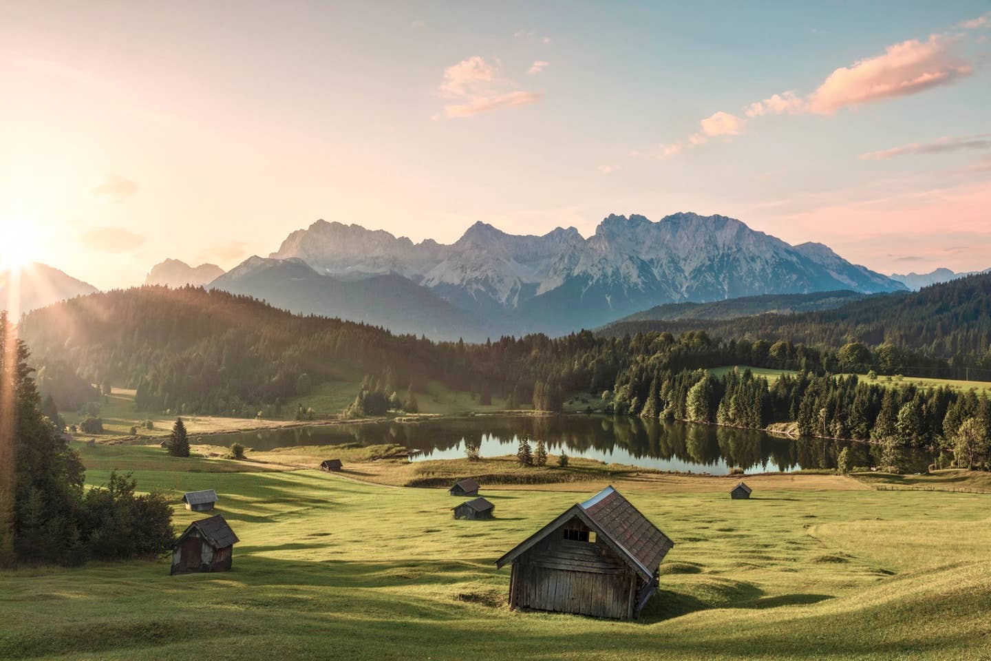 Urlaub Garmisch-Partenkirchen mit DERTOUR. Blick auf kleine Hütten und Scheunen vor dem Geroldsee bei Sonnenaufgang – im Hintergrund die Karwendel-Berggruppe