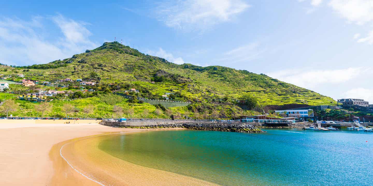 Ein Sandstrand in der Bucht von Machico auf Madeira, im Hintergrund ein grün bewachsener Hügel