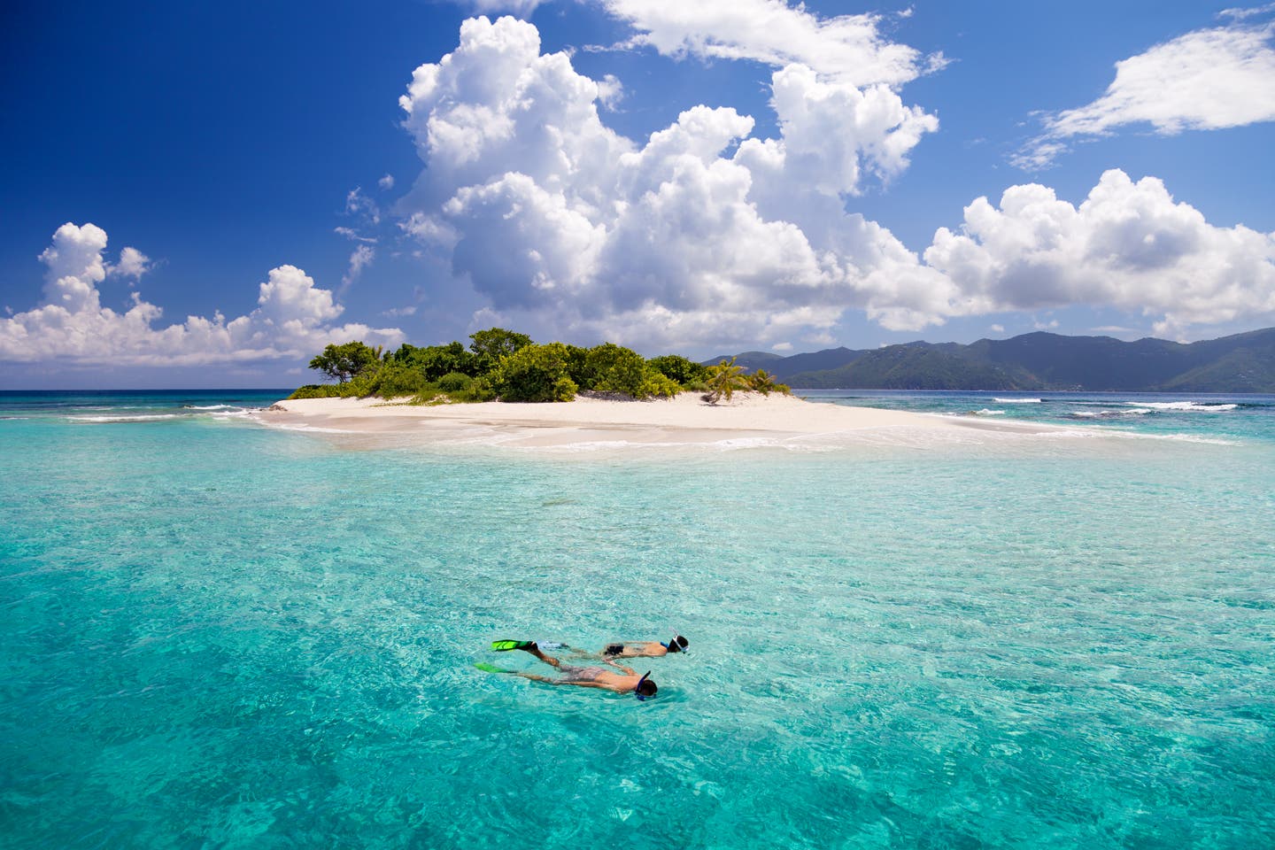 Paar taucht in der blauen See der Karibik, im Hintergrund eine Insel mit Strand