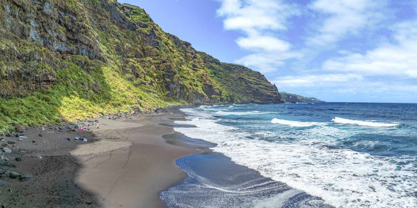 Schwarzer Vulkanstrand auf La Palma mit Atlantikwellen und grüner Steilküste