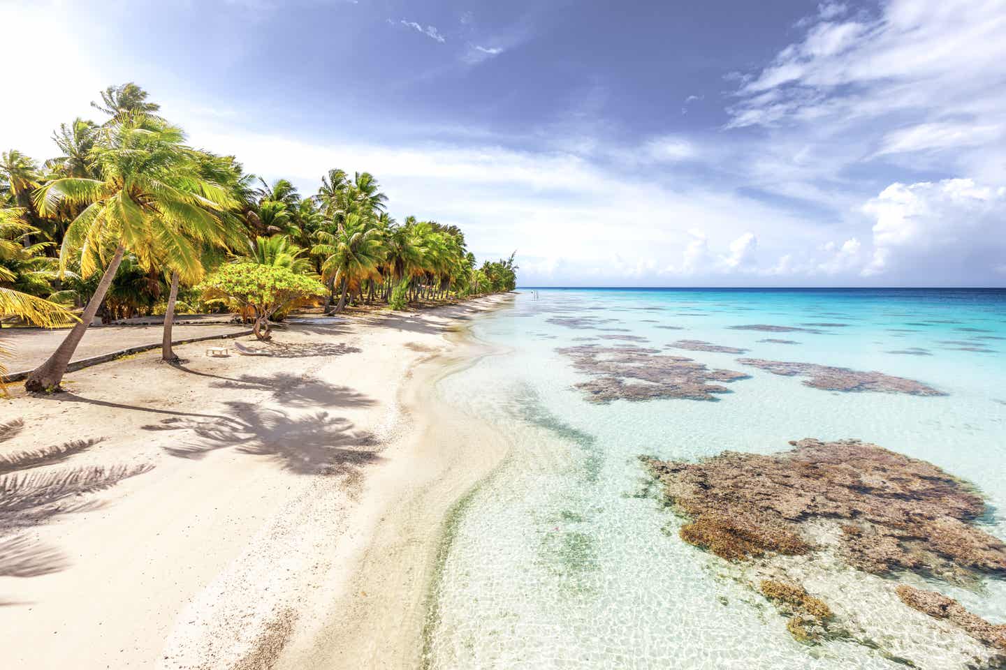 Blick auf einen weißen Strand mit türkisblauem Wasser, Felsen und grünen Palmen