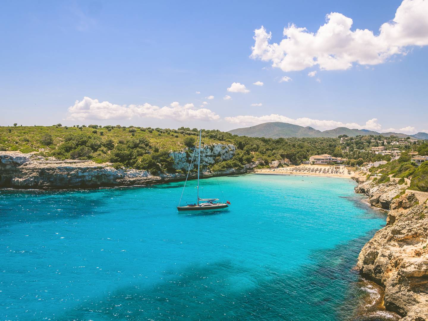 Mallorca-Urlaub am Strand von Estany, in der Bucht liegt ein einzelnes Segelboot Mallorca-Urlaub am Strand von Estany, in der Bucht liegt ein einzelnes Segelboot