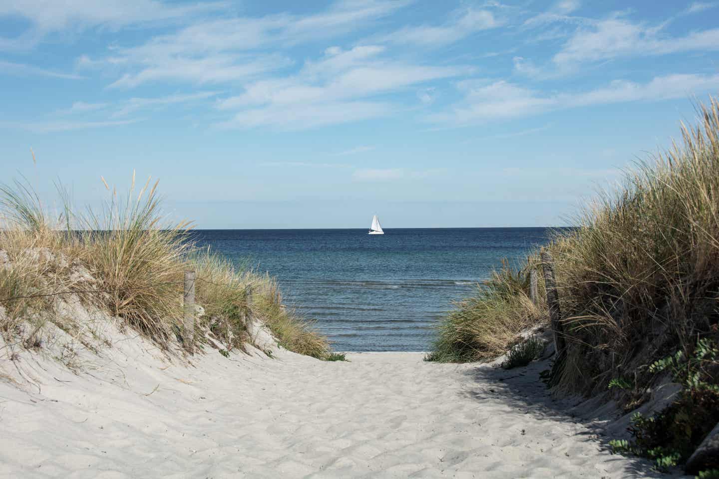 Reiseziele Ostern: Weg zwischen Dünen mit Blick auf ein Segelboot