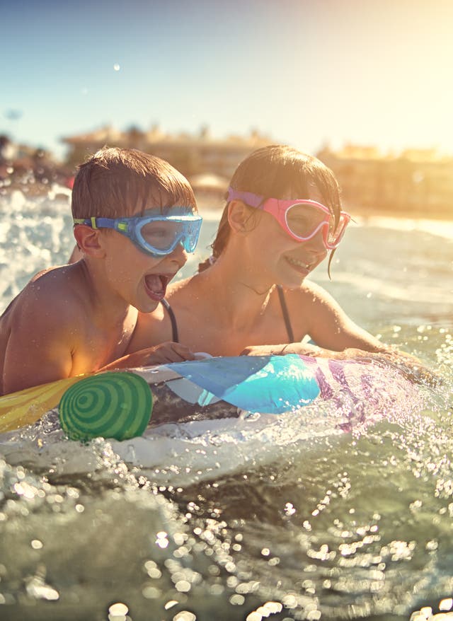 Familienurlaub Spanien Zwei Kinder mit Schwimmbrille spielen auf einer Luftmatratze im Meer beim Familienurlaub in Spanien